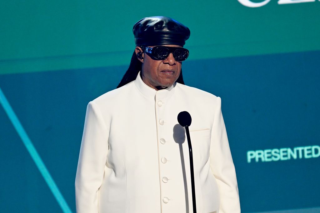 Stevie Wonder en veste blanche et chapeau noir sur scène devant le microphone