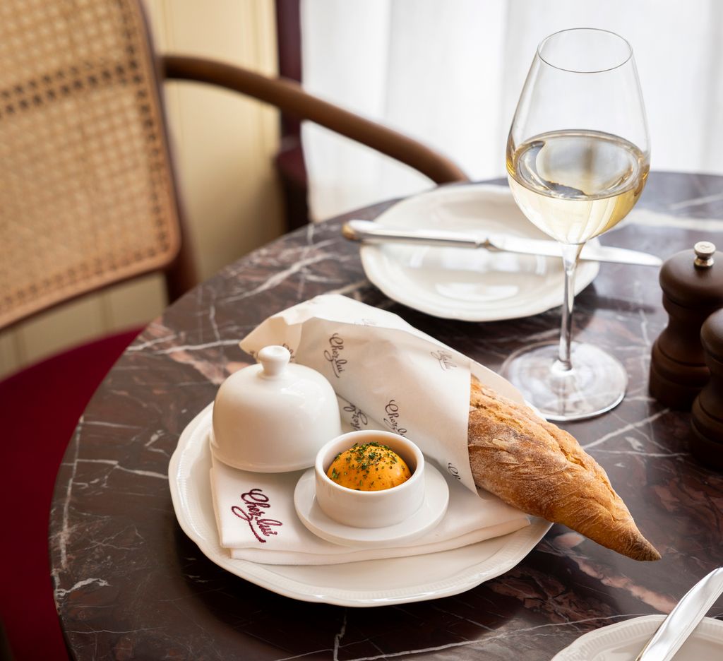 marble dining table with a french baguette on a with orange butter in a circle dish with a glass of wine positioned next to a plate