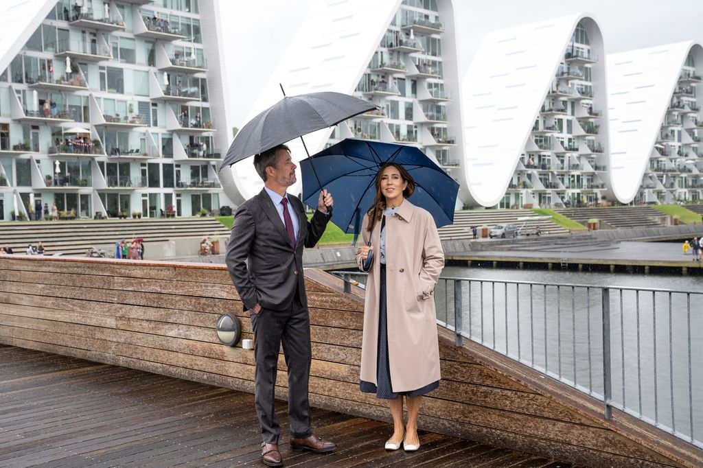 Queen Mary in a trench coat under umbrella with frederik