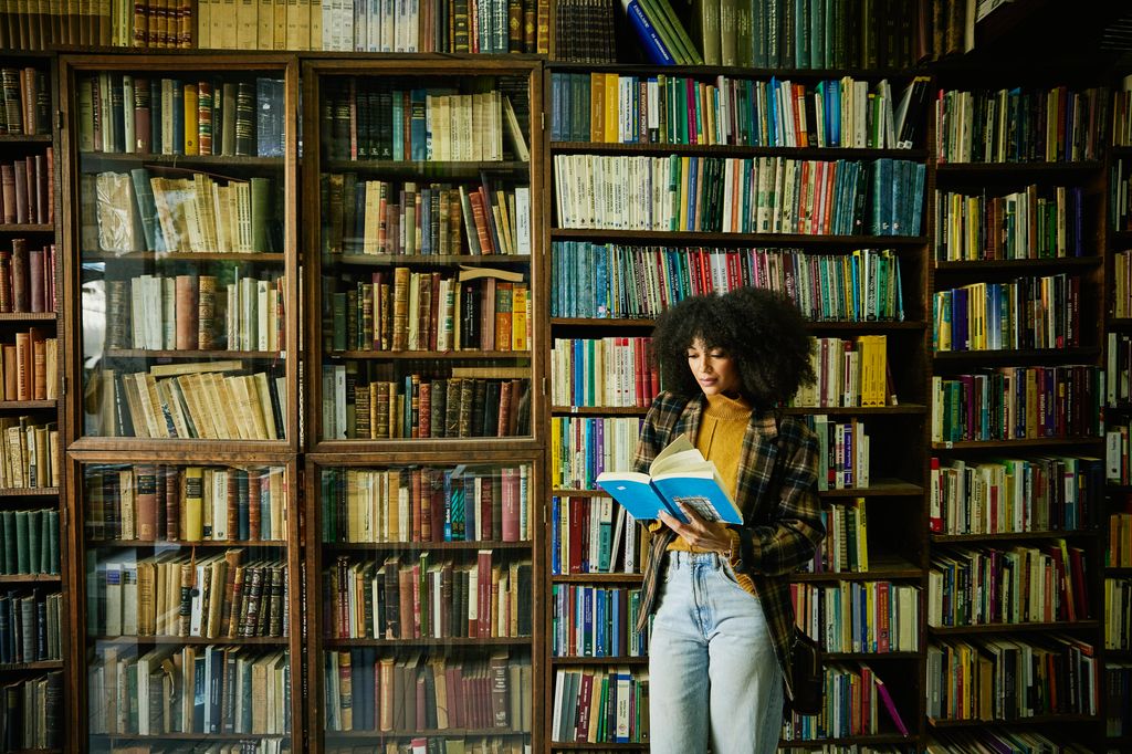 Wide shot of woman reading book while browsing in antique bookstore while exploring during city vacation