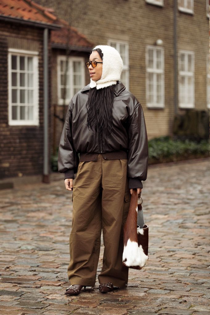 Amaka Hamelijnck wears wide brown pants, dark brown leather jacket, white hat and cow print bag outside the OpÃ©raSport show during the Copenhagen Fashion Week Autumn/Winter 2025 on January 27, 2025 in Copenhagen, Denmark