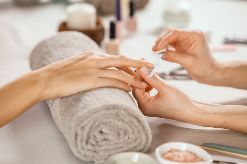 Close up shot of a woman in a nail salon receiving manicure by beautician with metal nail file. Woman getting nail manicure at spa centre. Beautician file nails to a customer in luxury salon