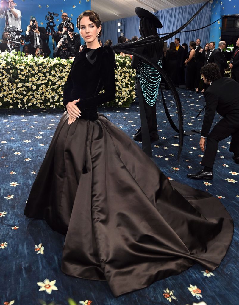 Lana Del Rey wears a black long sleeve gown with huge train and her hair in an updo
