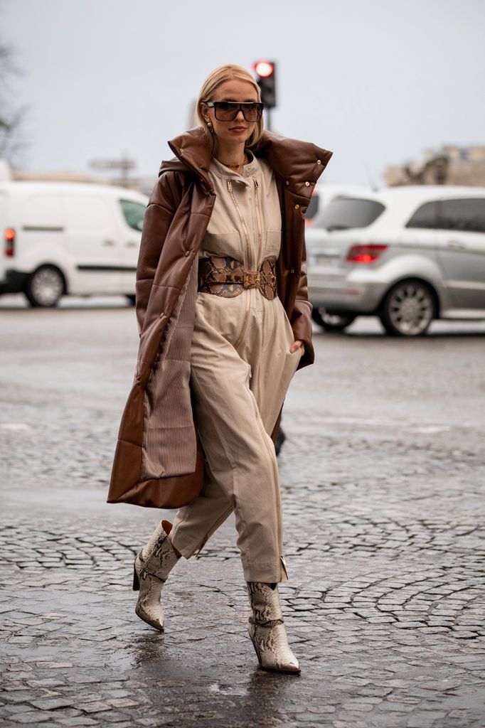 Leonie Hanne wearing beige jumpsuit with a statement belt, layered under a puffer coat, is effortlessly stylish. Paired with snakeskin boots, this look is functional and trendy. Perfect for a snowy day