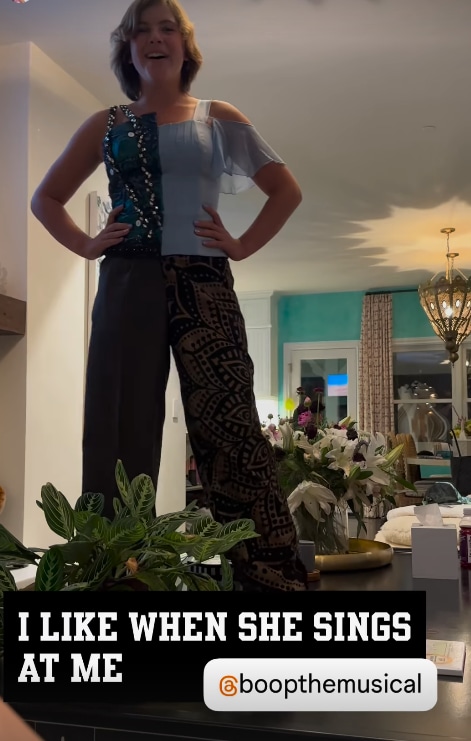 Pink's daughter Willow standing with her hands on her hips and singing while standing on the coffee table in her home with living room in the background