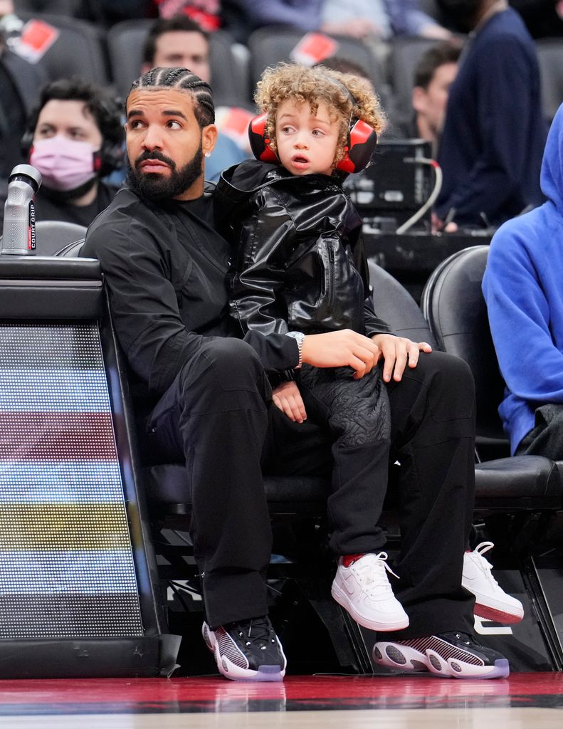 Drake sits with his son Adonis before the Toronto Raptors play the Philadelphia 76ers in their basketball game at the Scotiabank Arena on April 7, 2022 in Toronto, Ontario, Canada