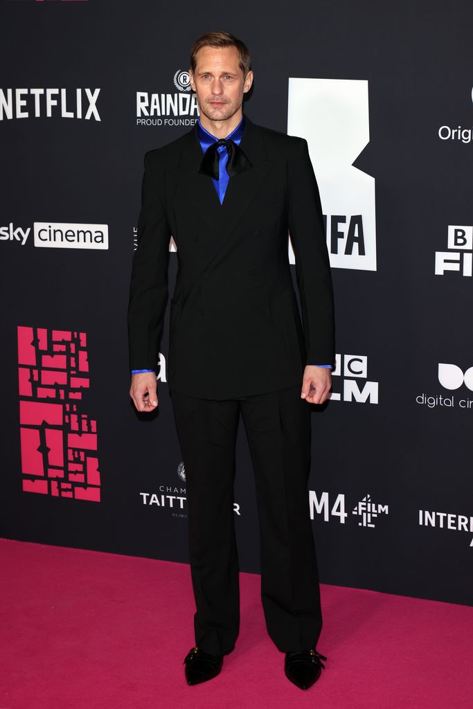 Alexander Skarsgard on pink carpet in black suit and blue shirt