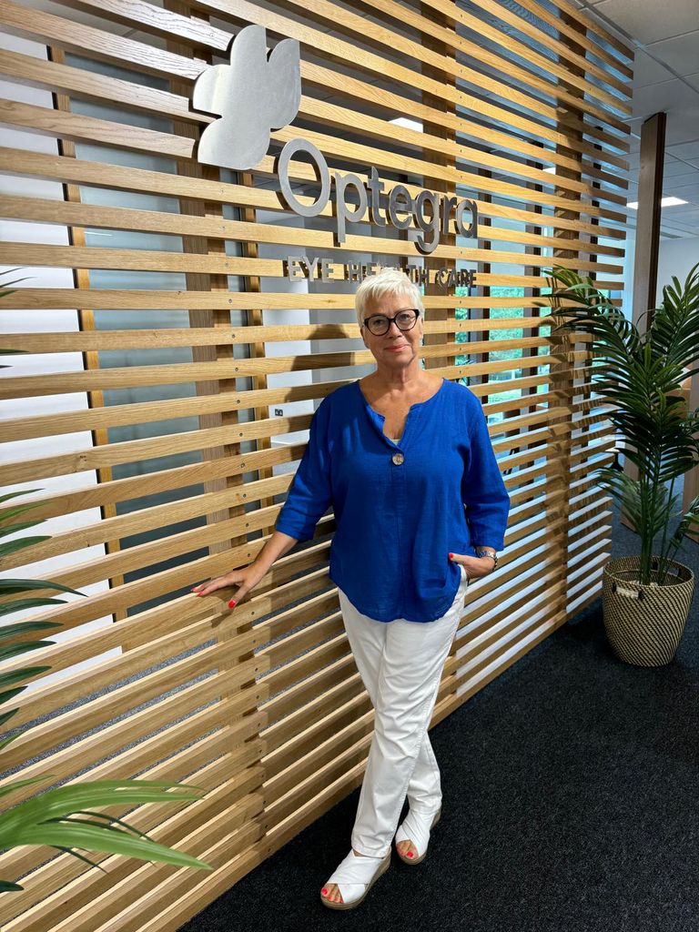 Denise Welch posing in a blue shirt with white jeans in front of a wooden panel