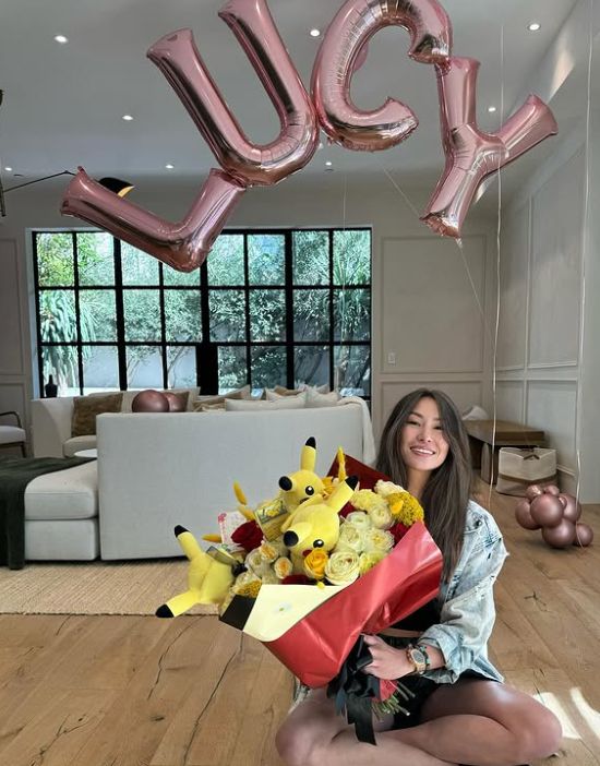Lucy Guo with balloons spelling out her name and a bouquet of flowers with Pikachu plushes