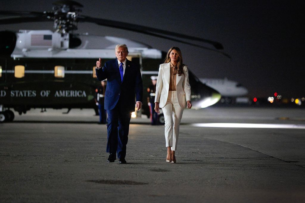 President Donald Trump  in navy suit and Melania Trump in white suit walking away from air craft after landing