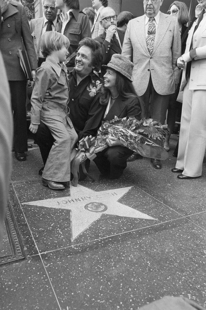 black and white photo of johnny cash and june carter cash bending down and smiling at son john on hollywood star on walk of fame