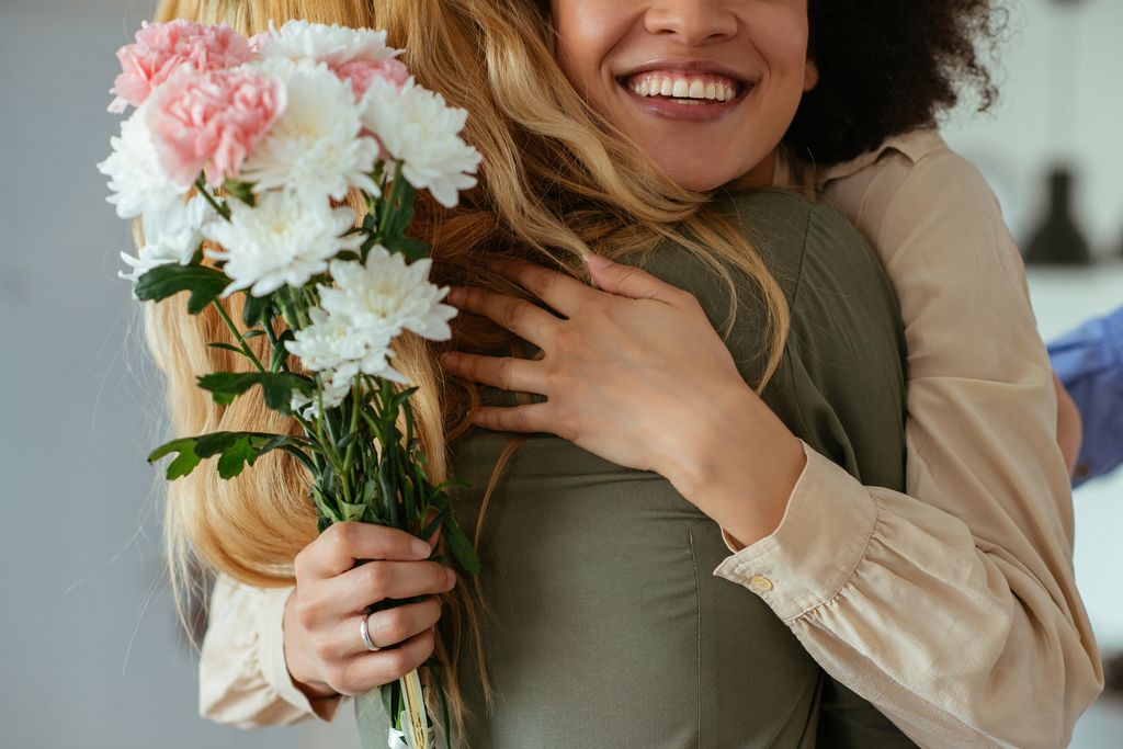 Portrait of two women hugging each other and holding flowers - for an article about gifts for burnout