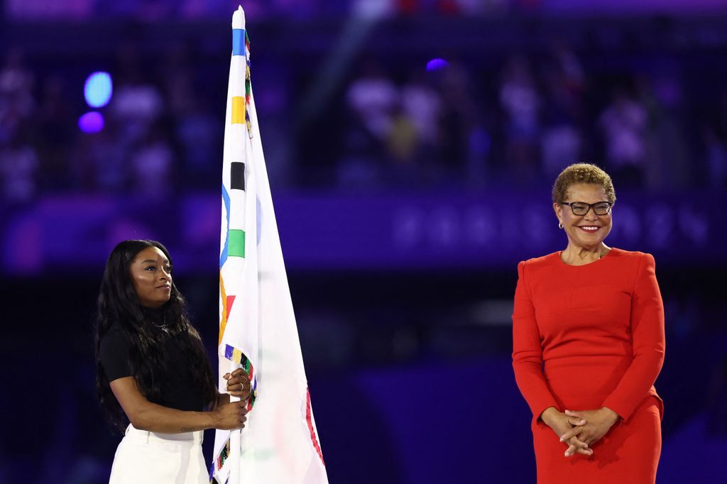 US' gymnasts Simone Biles holds the Olympic flag next to Los Angeles' Mayor Karen Bass during the closing ceremony of the Paris 2024 Olympic Games at the Stade de France, in Saint-Denis, in the outskirts of Paris, on August 11, 2024.