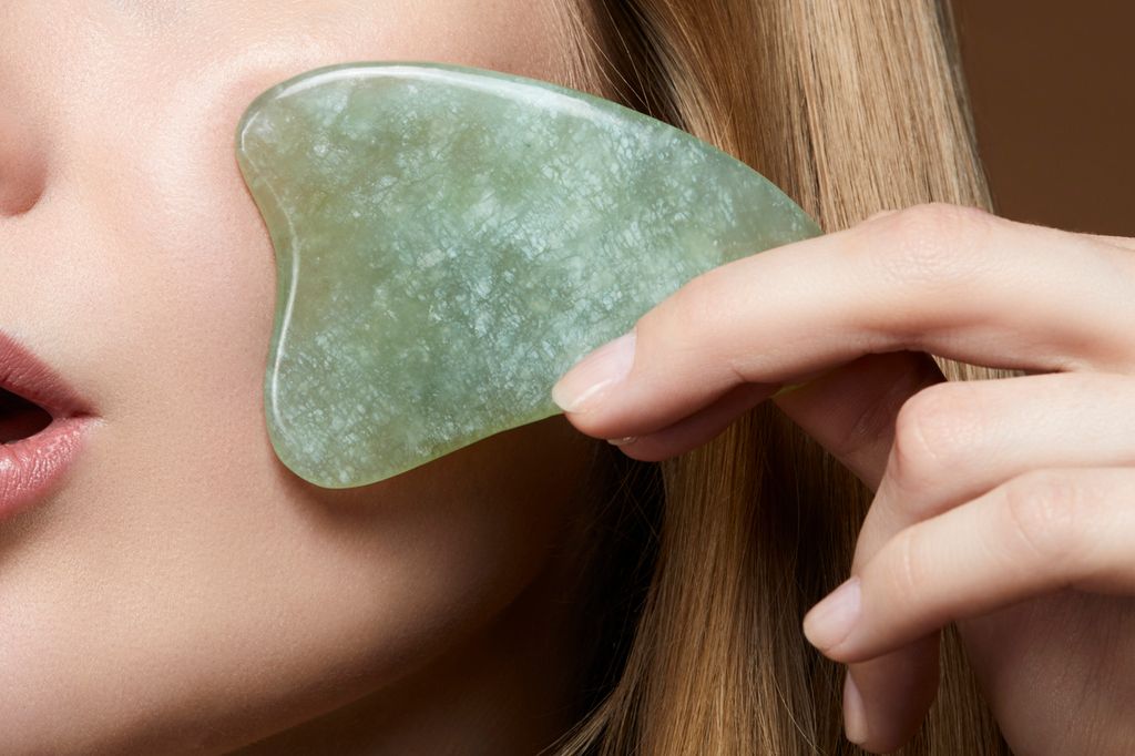 woman massaging her face to avoid wrinkles with a scraping jade Gua Sha Massage tool- asian skin care beauty trend