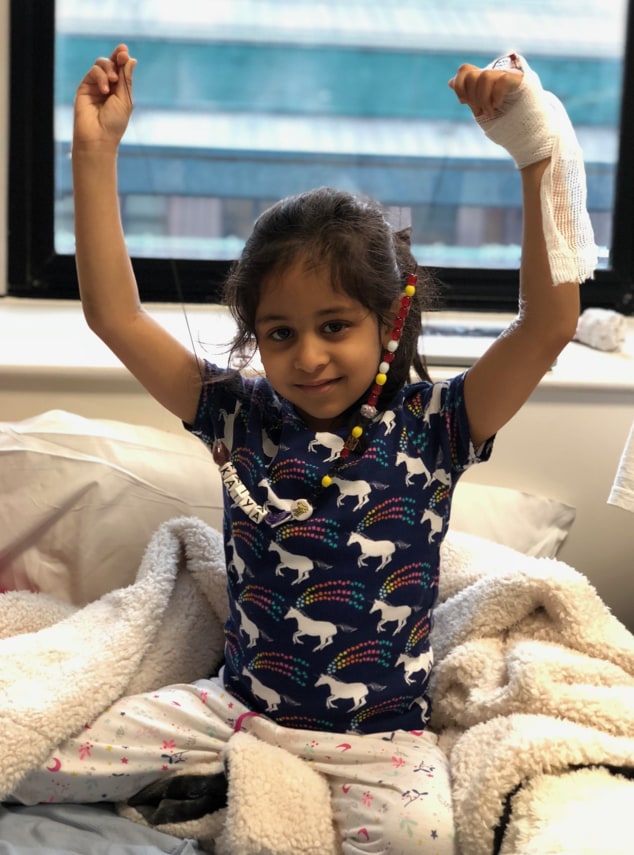 child in hospital bed with arms raised