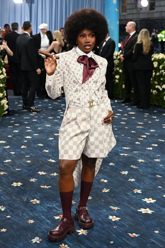 Doechi wears a Louis Vuitton logo emblazoned suit, with shorts, chunky Mary Jane shoes and knee high marron socks.