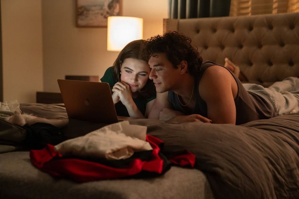 Two people watch a laptop screen in bed