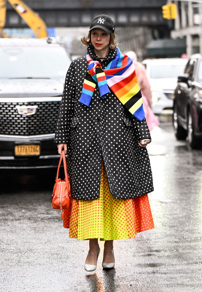 Chloe King is seen wearing a Polkadot coat, yellow and orange polkadot dressed, white heels, orange bag and New York Yankees baseball cap outside the Brandon Maxwell show during NYFW F/W 2025 on February 06, 2025