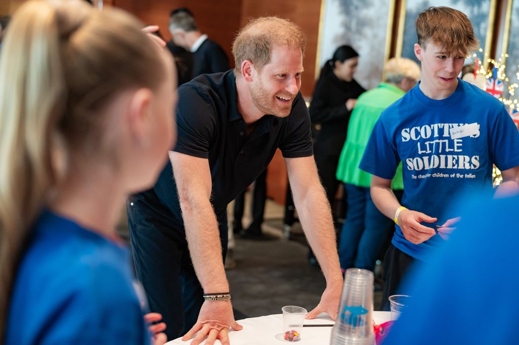 Prince Harry leaning on a table with a group of young people in blue shirts