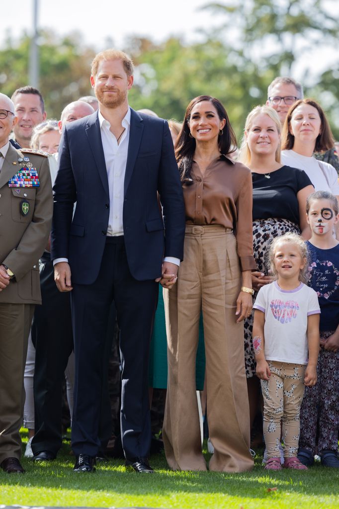 Meghan in all brown beside prince harry in crowd