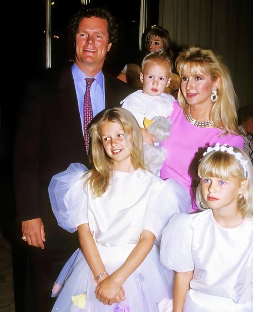 Rick Hilton stands behind daughter Nicky, dressed in a white bridesmaid dress, with sister Paris next to her. Kathy Hilton stands in a pink dress holding her young son Barron.