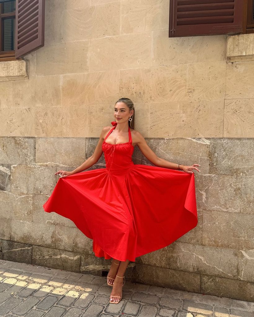 Zara McDermott poses against a wall in red dress in Majorca
