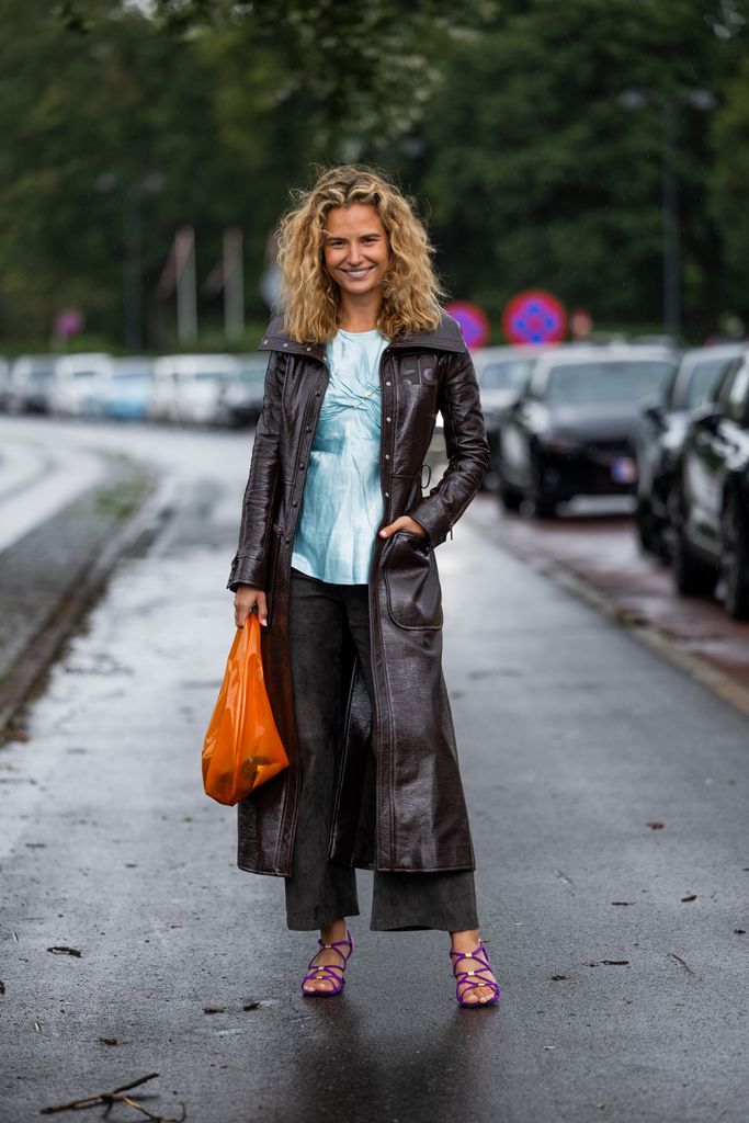 Mija Knezevic wears brown coat, orange bag, turquoise bag, denim jeans, purple sandals outside Saks Potts 