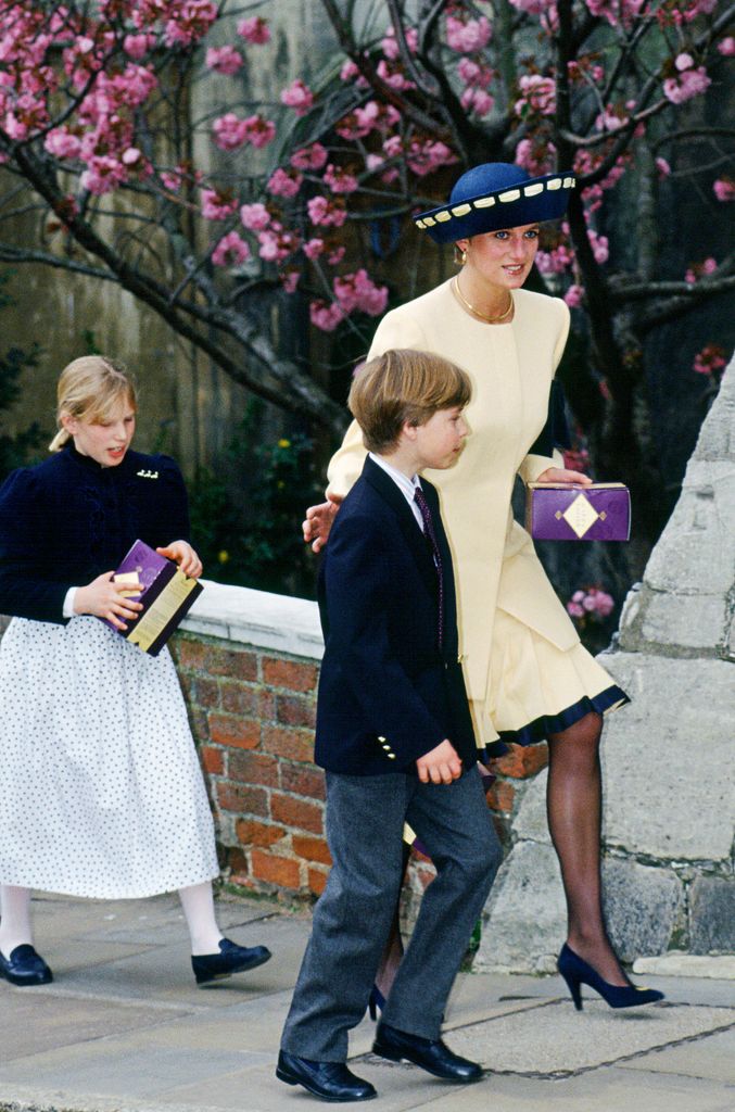 Princess Diana walks up the steps with Prince William and Lady Louise Windsor, dressed in her yellow pleated suit and navy heels, framed by pink cherry blossoms and Easter boxes in hand.