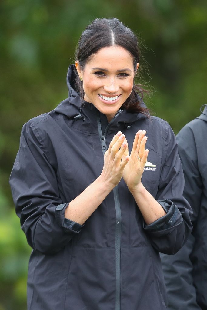 Meghan Markle clapping in a raincoat