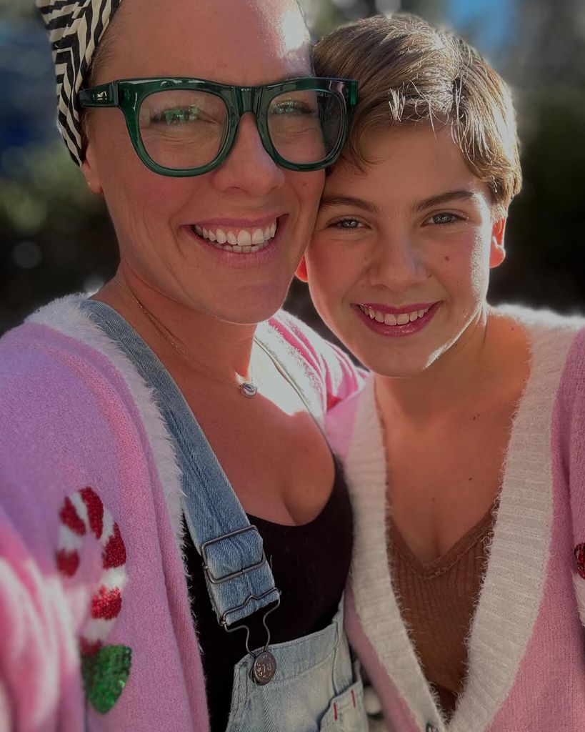Pink wearing black top, dungarees and pink cardigan smiles as she takes selfie with her daughter Willow wearing same pink cardigan