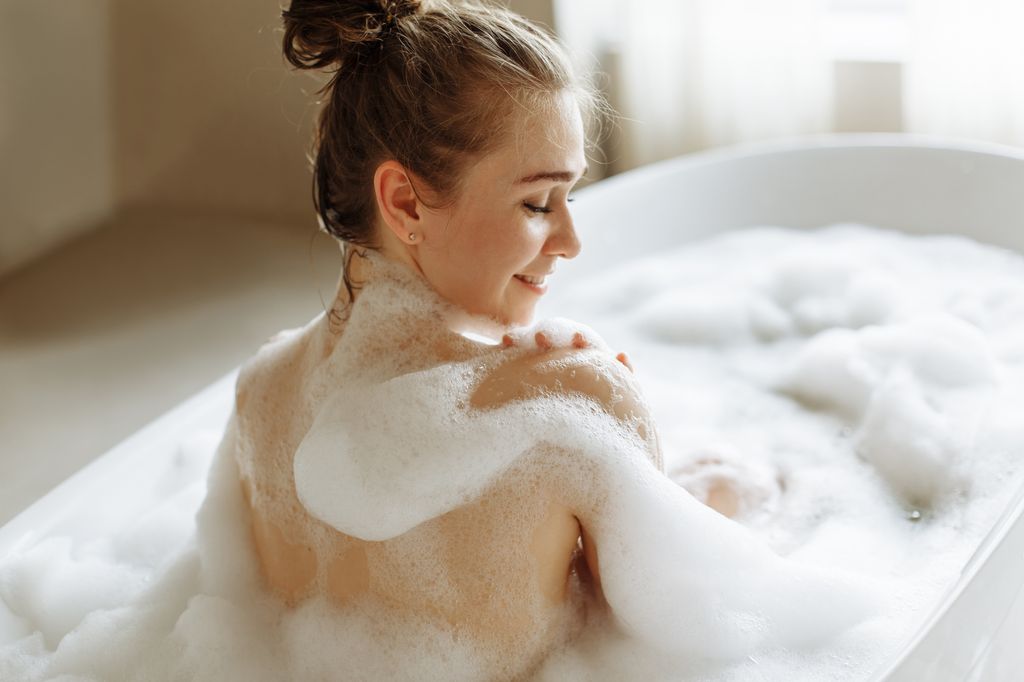 Young handsome man in wireless headphones relaxing in bath with foam and  enjoying music Stock Photo