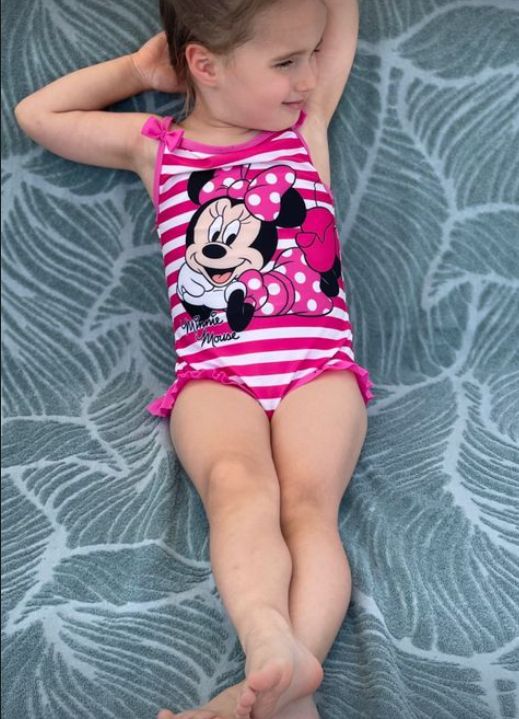 A young girl relaxing with arms behind her head in a pink Minnie Mouse costume