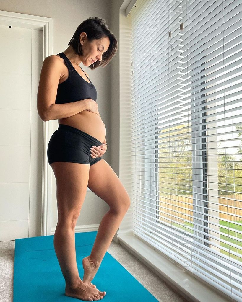 janette manrara holding baby bump posing in black sports bra and trousers