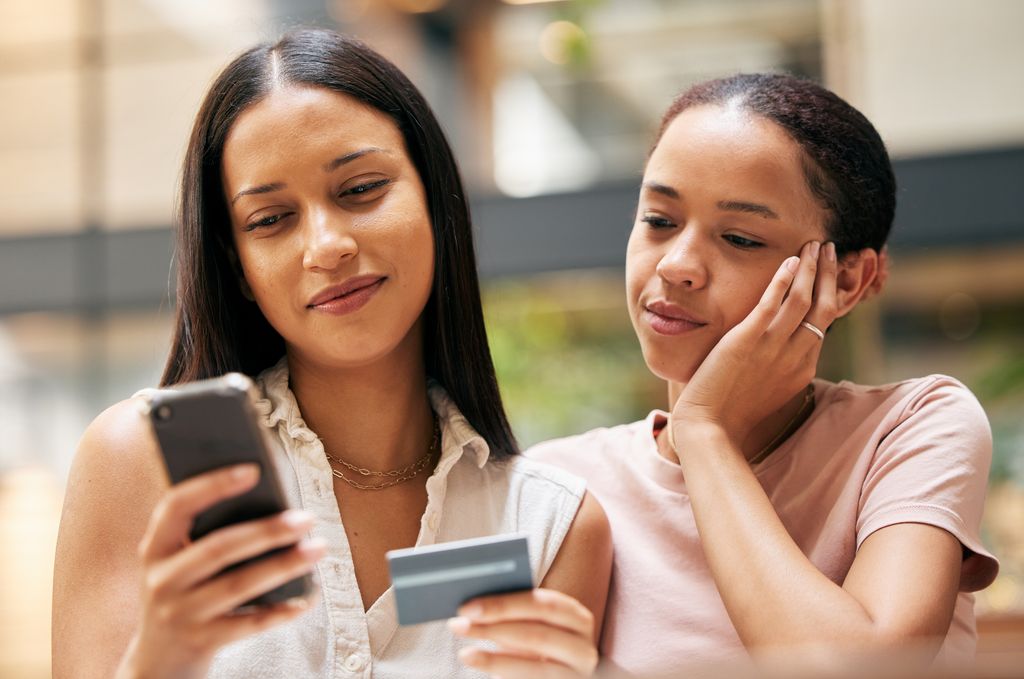 Woman looking at phone with credit card in hand and daughter watching