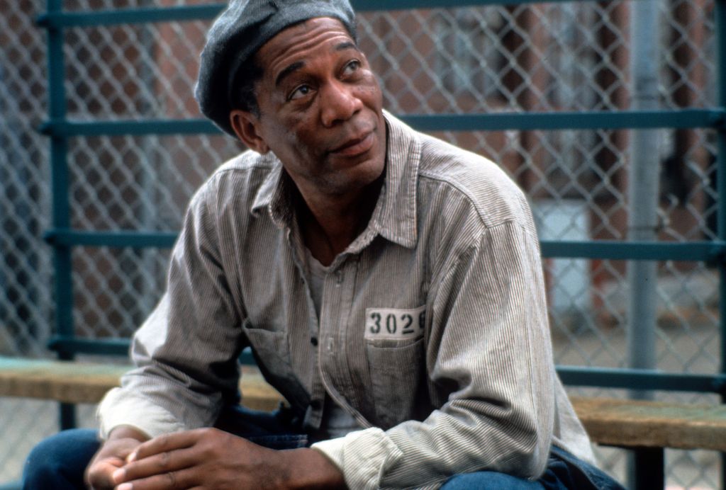 Morgan Freeman sitting outside with a hat and prison uniform on in a scene from the film 'The Shawshank Redemption', 1994.