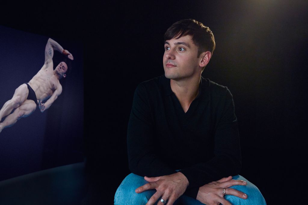 Tom Daley in a black jumper looking at a picture of himself diving