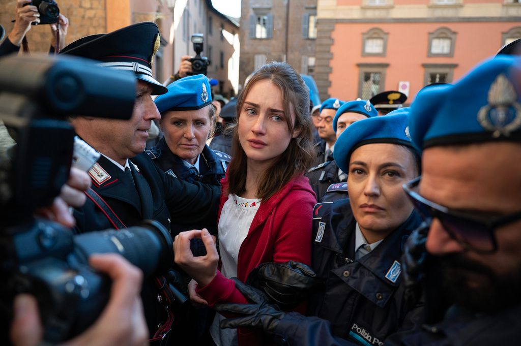 brunette woman walking through crowd of people with cameras