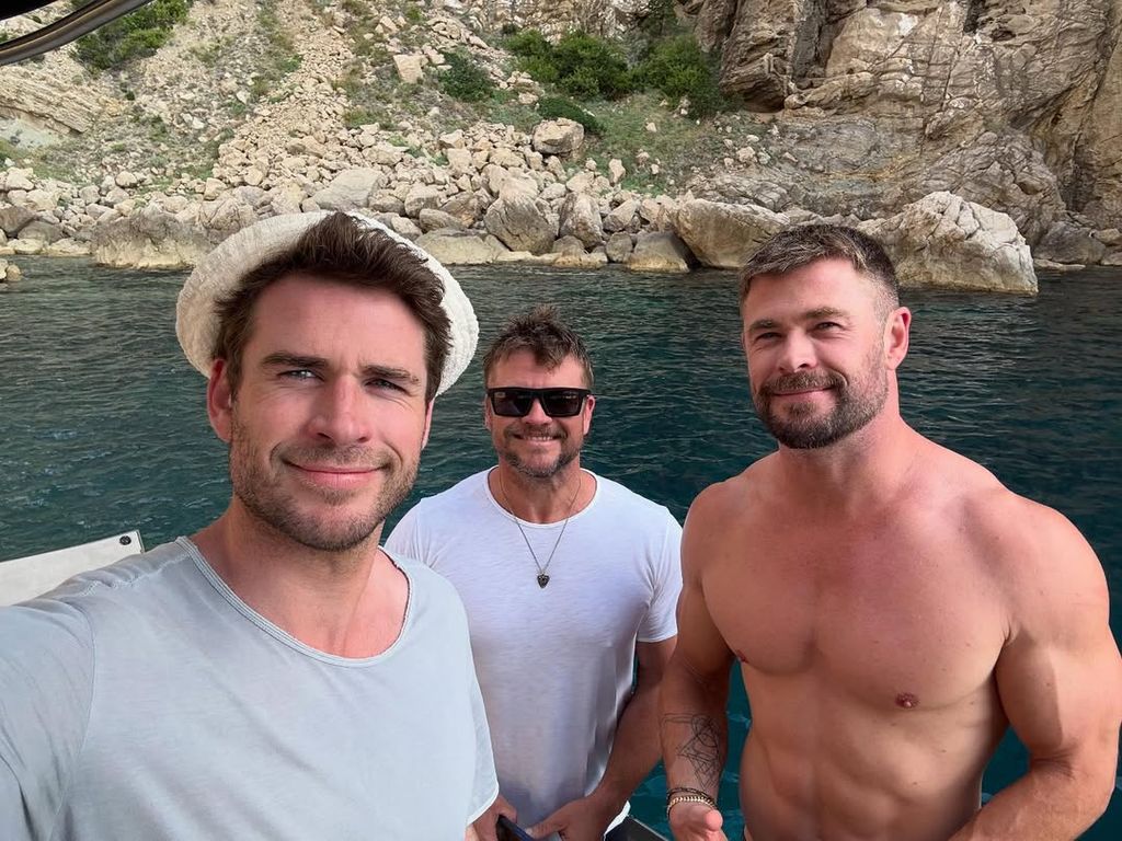 liam, chris, and luke hemsworth posing on boat in front of lake