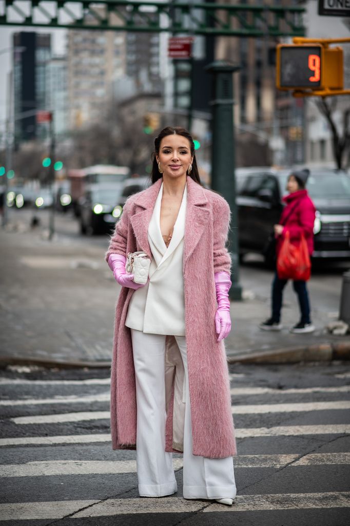 Un invité de la NYFW pose dans la rue dans un costume blanc et un manteau rose