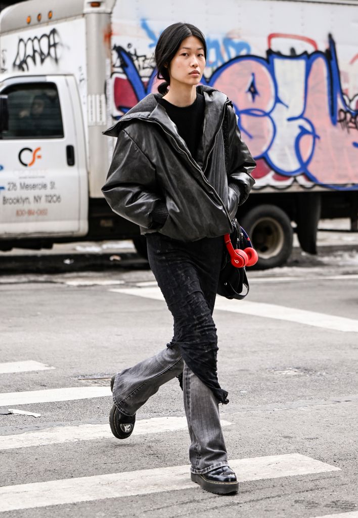 A model is seen wearing a black puff jacket, black lace skirt, black boots and black bag outside the Kallmeyer show