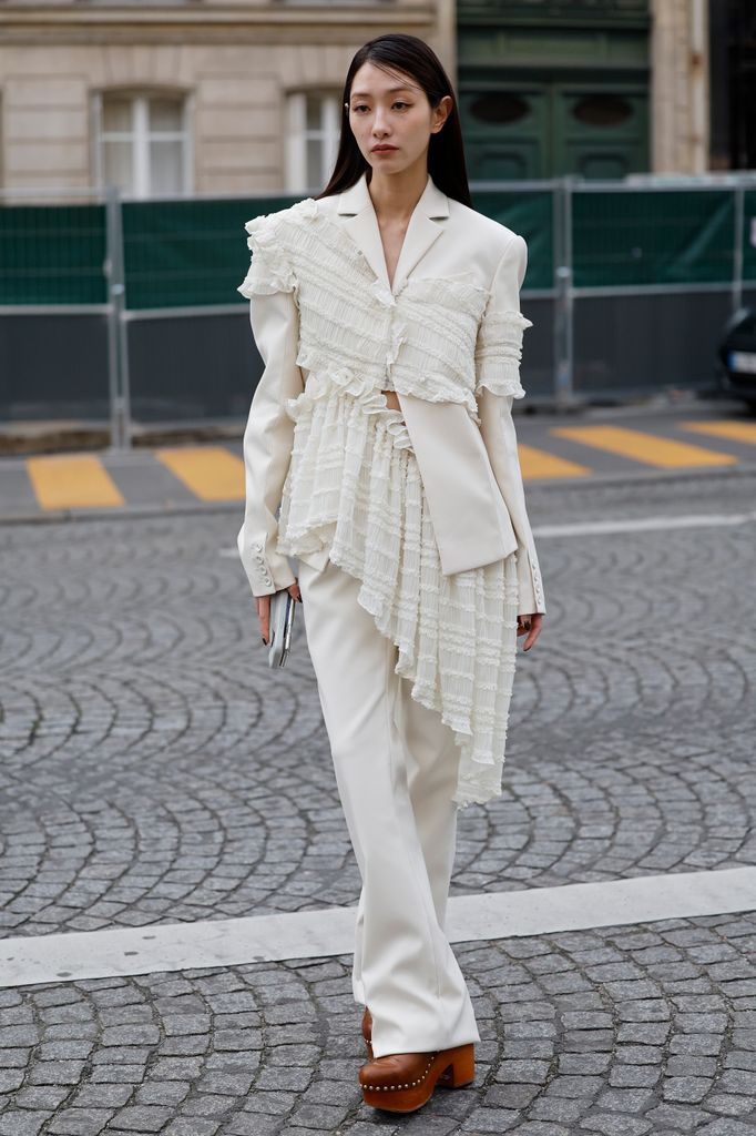 A guest wears cream blazer with ruffle details, matching trousers, brown mules, outside Rokh, during the Womenswear Fall/Winter 2025/2026