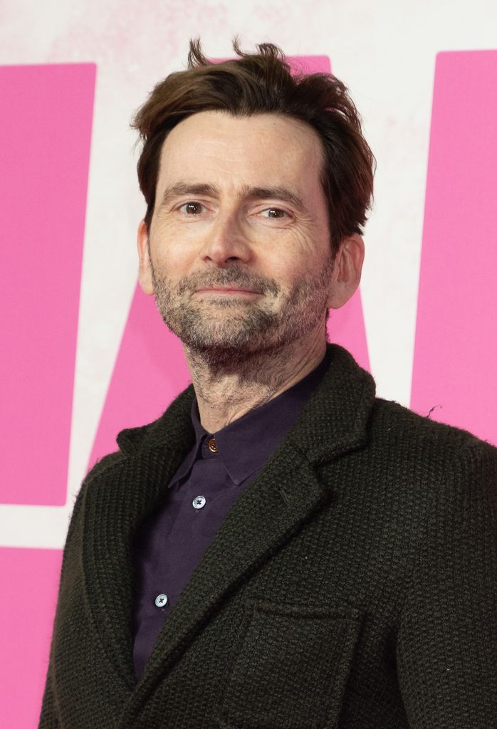 David Tennant in a suit in front of a pink and white background