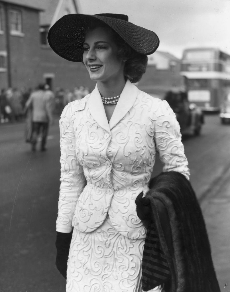 16 de junho de 1953: No primeiro dia da reunião do Royal Ascot, a modelo Fiona Campbell Walter (mais tarde Baronesa von Thyssen) usa um chapéu de palha preto, um terno branco com cordão e colar de pérolas e carrega uma estola de pele.  (Foto de Keystone/Getty Images)