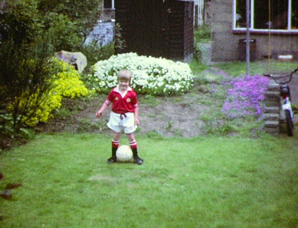 A young David Beckham in red shirt and white shorts with a football