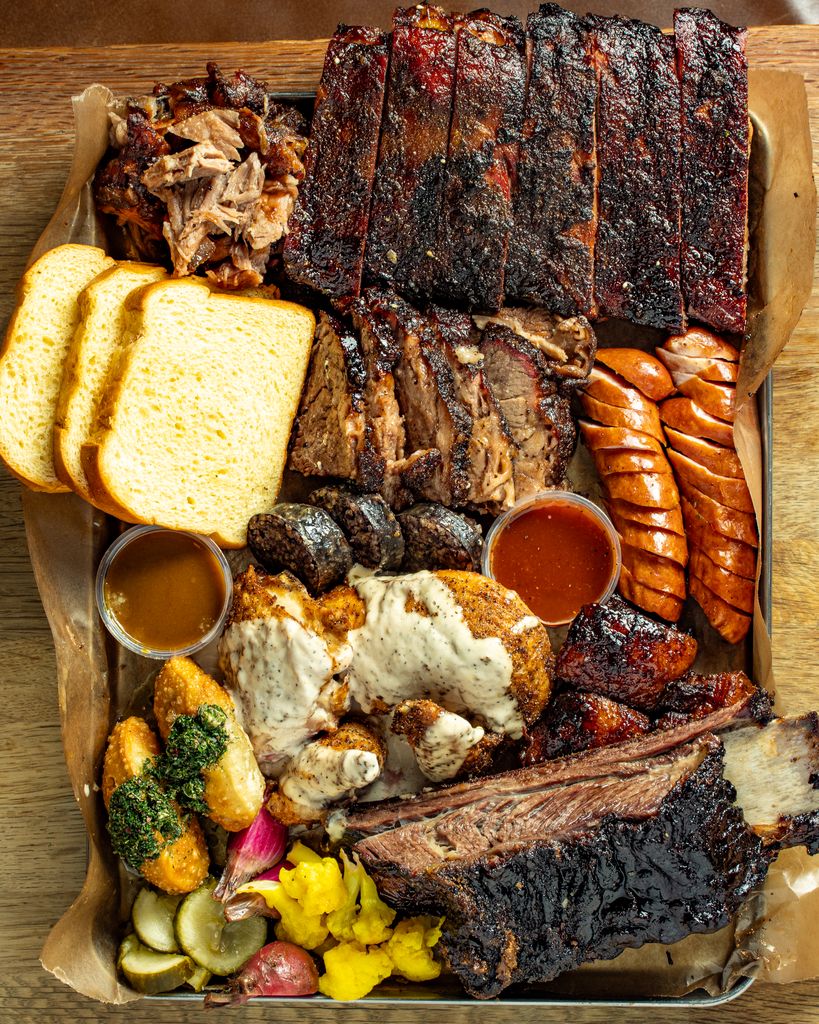 An overflowing BBQ platter at Red Dog Saloon in London featuring ribs, brisket, pulled pork, sausage, and chicken with traditional sides like pickles and Texas toast.