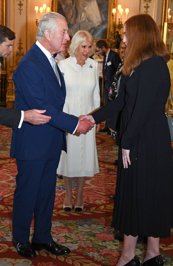 King Charles III in navy suit and Queen Camilla in white meeting people