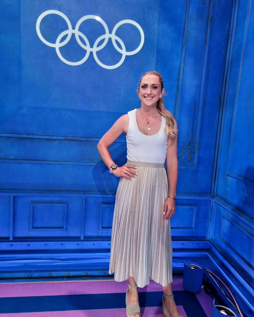 Laura Kenny in a white top and metallic skirt in front of the olympics logo