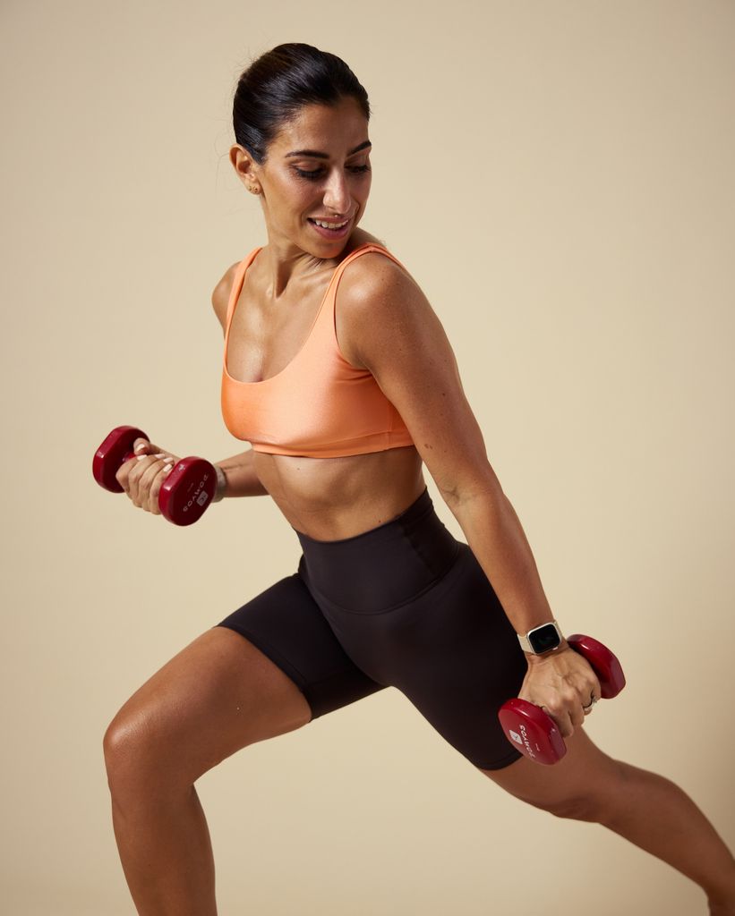 Woman in apricot coloured crop top and black shorts lifting weights