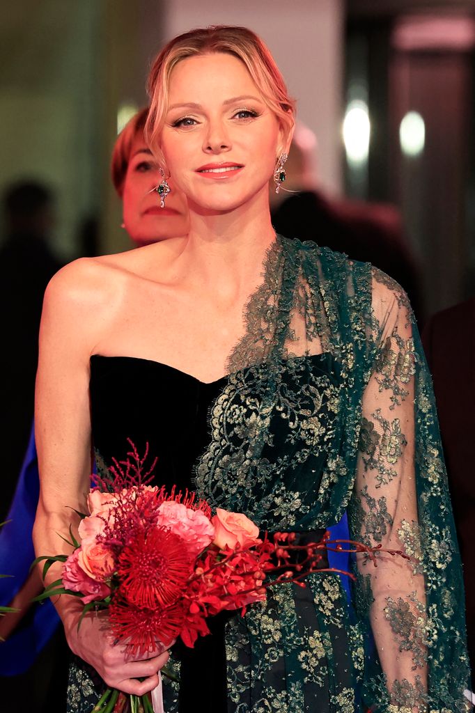 Princess Charlene of Monaco posed in a black dress with a green embroidered shawl while holding a bunch of roses.