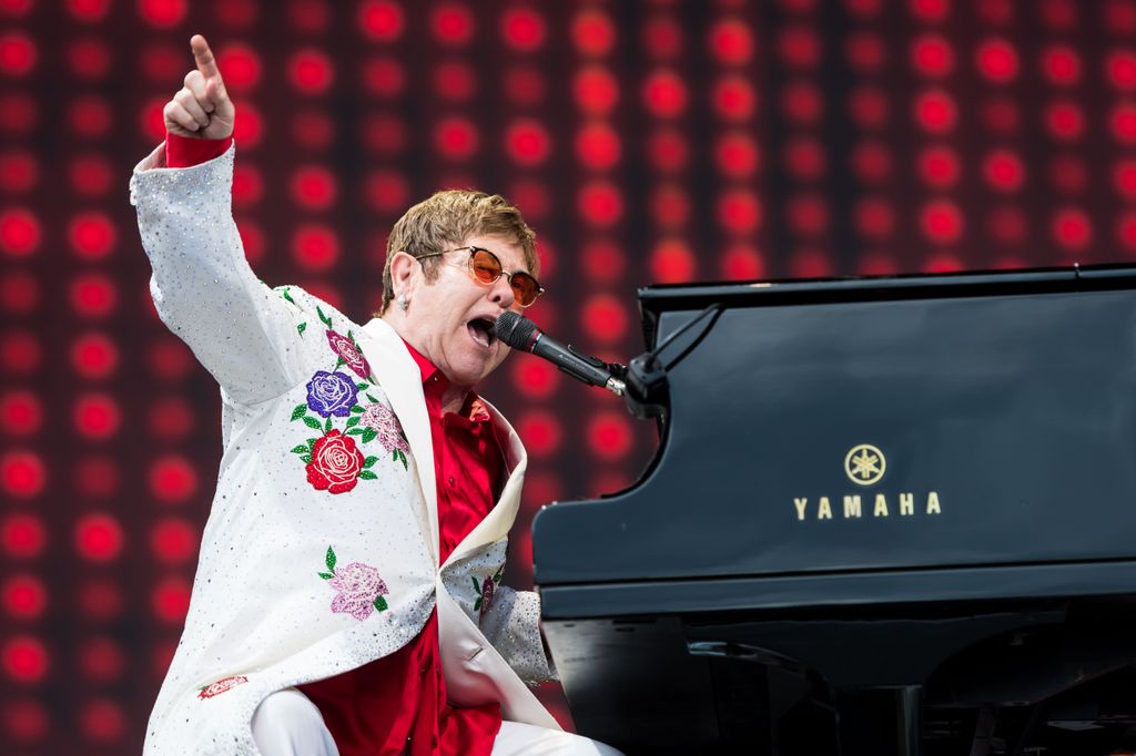Elton John  sits at a pianp and points at the audience as he performs live at Twickenham Stoop 